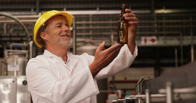 Mature brewer dressed in white lab coat and safety helmet carefully inspecting a beer bottle on the production line. Ideal for use in topics related to quality control, brewery operations, manufacturing process, beer industry, industrial work environment, safety protocols, and expertise in production. Perfect for illustrating content about brewing processes, worker satisfaction, and industrial craftsmanship.