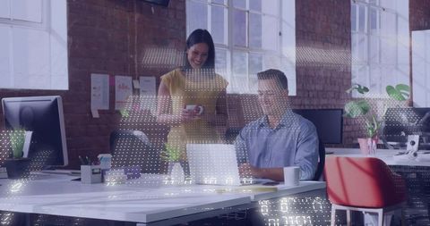Collaborating coworkers using laptop and smartphone in open-plan industrial loft office