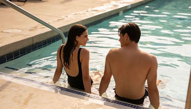 Young couple relaxing and chatting on pool steps during sunny summer afternoon