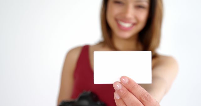 A young Caucasian woman is smiling and holding a blank card in front of her, with copy space. Her cheerful expression and the card offer a perfect opportunity for customization in advertising or personal messaging.