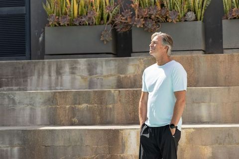 Middle-aged man standing on concrete steps looking up near succulent planters in sunlight