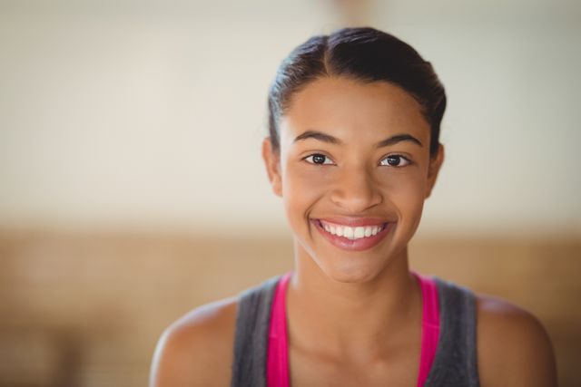 High school girl smiling confidently while standing in a basketball court. Ideal for use in educational materials, sports promotions, youth programs, and advertisements focusing on healthy lifestyles and fitness.