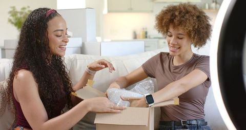 African american friends unboxing parcel together on couch using ring light for content