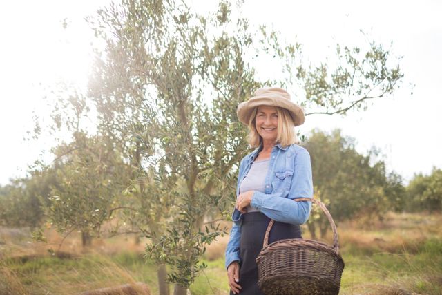 Portrait of happy of woman standing with basket in olive farm on a sunny day