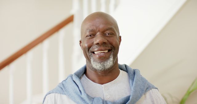 Portrait of happy senior african american man with grey beard smiling in hallway at home. Retirement, wellbeing, domestic life, and senior lifestyle, unaltered.