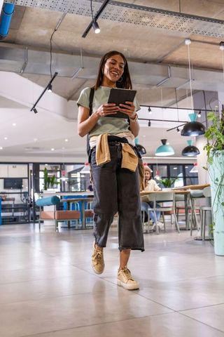 Young woman walking through modern coworking space holding tablet and smiling
