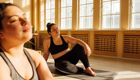 Plus-size woman practicing yoga in sunlit studio resting after stretching session