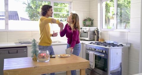 Couple Reaching Hands Over Kitchen Island Sharing Mug and Smartphone