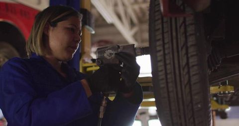Female Mechanic Using Impact Wrench Changing Tire on Lift in Auto Repair Garage