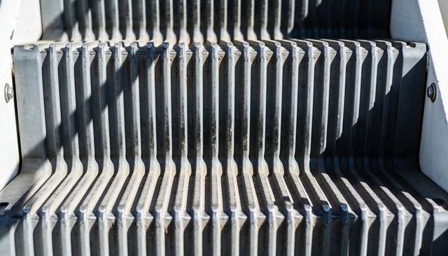 Sunlit weathered metal escalator treads with ribbed grooves and shadow patterns