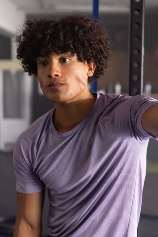 Young man pausing between sets at gym wearing purple tee, focused athlete portrait