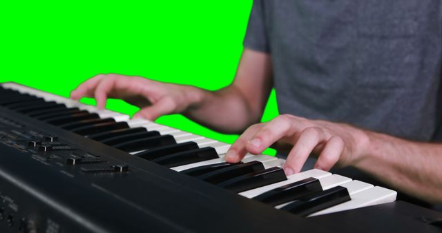 Person playing electric keyboard against green screen background. Exhibits musician's hands pressing keys on electronic piano keyboard. Green screen allows for versatile usage, such as inserting into various video or photo projects. Ideal for music tutorials, educational materials, promotional content for music-related events or products, and multimedia art endeavors.