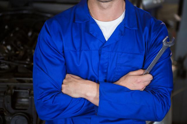Mid section of mechanic standing with arms crossed at repair garage