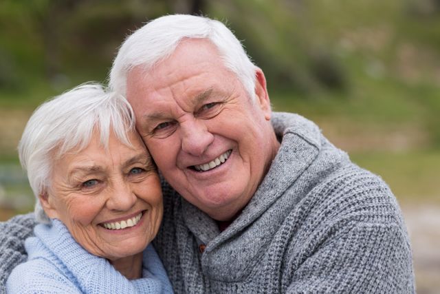 Elderly couple smiling and embracing outdoors, showcasing love and togetherness. Ideal for use in advertisements, retirement planning materials, healthcare promotions, and lifestyle blogs focusing on senior living and relationships.