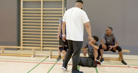 Coach leading diverse male athletes during team huddle resting and discussing in gym court