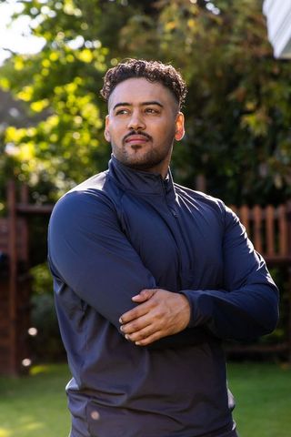Sunlit african american man standing in backyard wearing navy athletic jacket contemplative