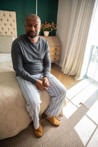 Senior african american man sitting on bed in morning light practicing mindful rest