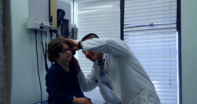 Doctor examining young boy's ears in a medical office. The image is useful for articles or advertisements related to healthcare, pediatric care, child health, medical exams, and doctor visits.