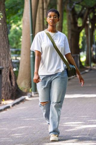 African american woman walking wearing white tee ripped jeans and olive crossbody bag
