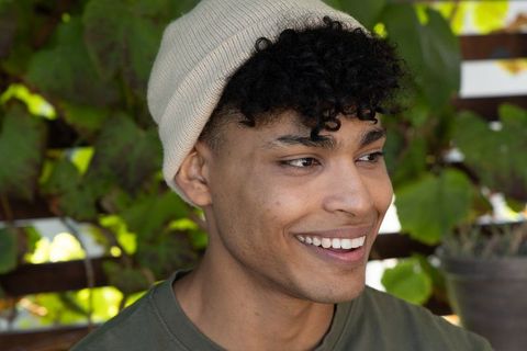 Young african american man smiling outdoors wearing beanie and olive shirt