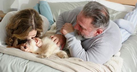 Puppy Cuddling With Mature Couple on Cozy Bed Showing Intimate Pet Bonding and Warmth at Home