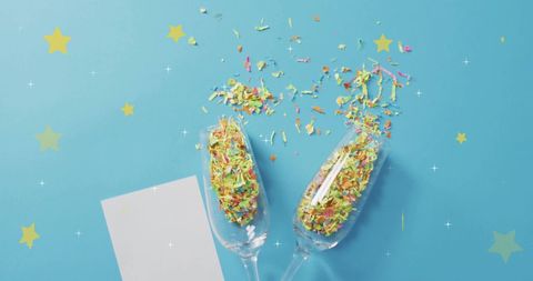 Celebratory confetti and champagne glasses on blue background