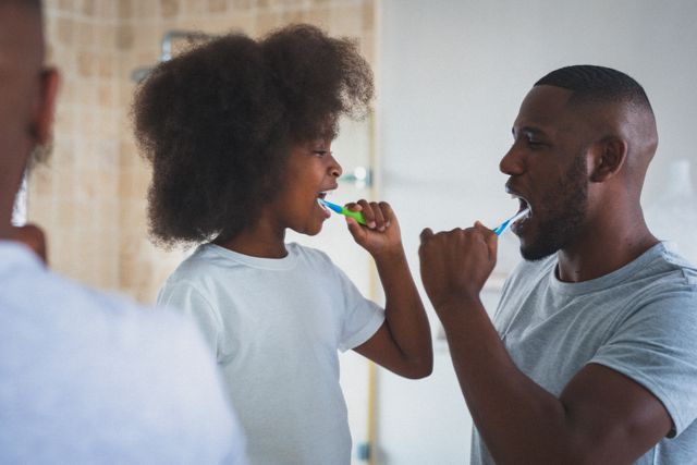 Happy african american girl and her father brushing their teeth together in the bathroom. staying at home in isolation during quarantine lockdown.