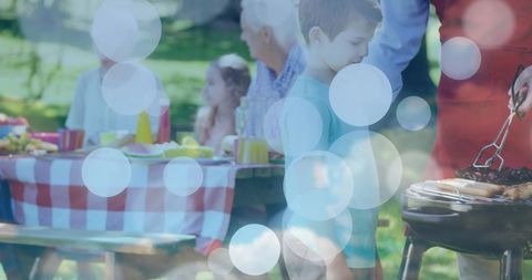 Multigenerational family picnicking in park with woman grilling backyard barbecue joy