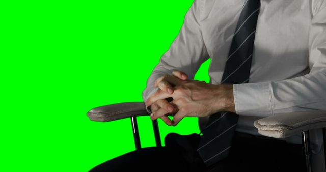 Businessman clasping hands while sitting in chair against green screen backdrop. Ideal for use in corporate or business-related content, presentations, and promotional materials. Perfect for illustrating professional meetings, interviews, or business scenarios. The green screen background makes it easy to integrate into various visual projects.