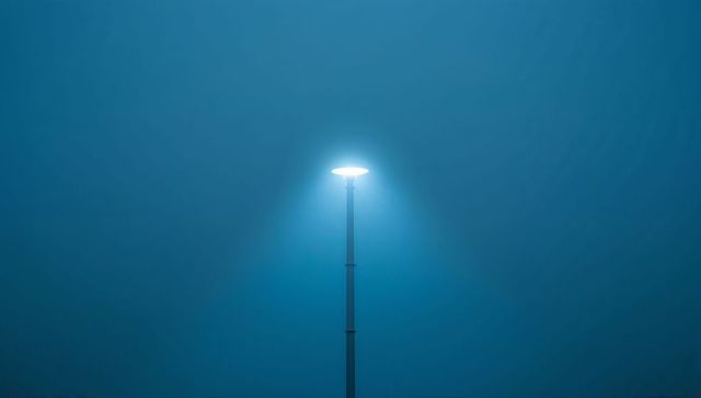 Solitary streetlamp casting cool white beam through foggy night minimalist halo moody glow
