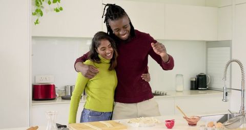 African American Man and Indian Woman Embracing While Preparing Pasta on Kitchen Island