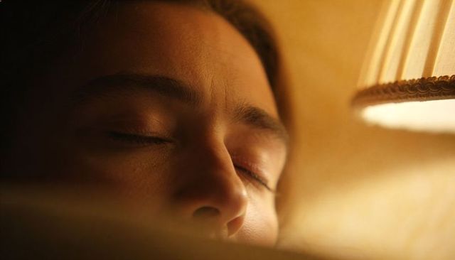 Woman resting under warm lamp light, close-up cozy bedtime portrait with amber glow