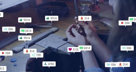 Jeweler filing metal at workbench with social media notification overlays, artisan craft