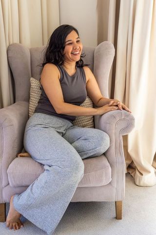 Smiling woman relaxing in cozy corduroy wingback chair wearing gray loungewear at home