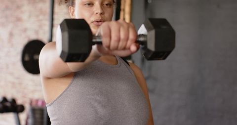 Woman lifting hex dumbbell during focused strength training session in industrial gym studio