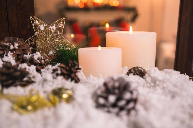 Candles and pine cones are placed on fake snow, creating a cozy and festive atmosphere. A star ornament adds a touch of sparkle. Ideal for holiday-themed promotions, greeting cards, or home decor inspiration.