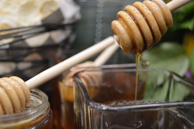 Close-up view showing honey dripping from a wooden dipper into a glass jar. Perfect for concepts related to healthy eating, organic food, natural sweeteners, and cooking ingredients. Suitable for use in articles, blogs, or advertisements focusing on natural foods, recipes, and healthy lifestyle.