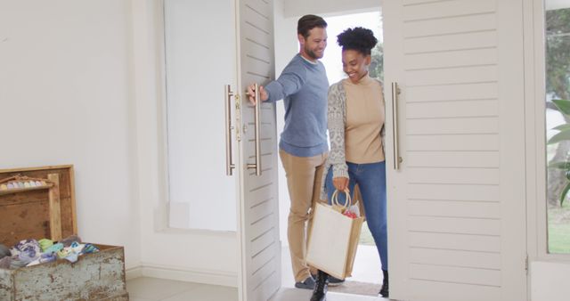 Image of happy diverse couple walking into house with shopping bags. Love, relationship and spending quality time together at home.