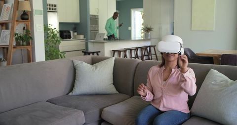 Woman Wearing VR Headset on Couch While Partner Using Phone in Modern Open-Plan Living Space