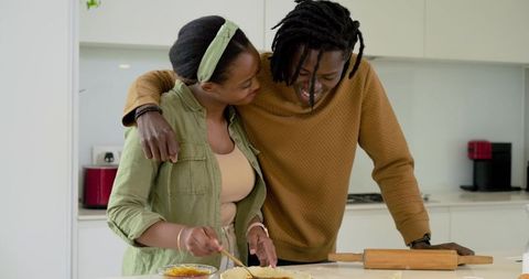 African american couple baking together in bright kitchen smiling while preparing pastry