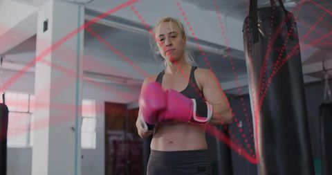 Female boxer adjusting pink gloves and preparing for punching bag workout in gym