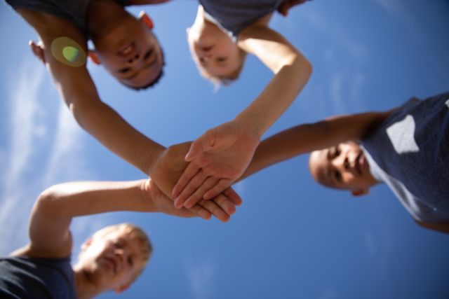 Directly below shot of multiracial elementary schoolboys stacking hands while standing against sky. unaltered, childhood, education, sports training, team sport and sports activity concept.