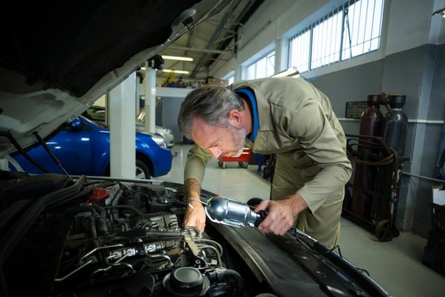 Mechanic examining a car with lamp in repair garage
