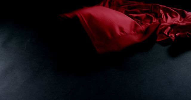 A red fabric is elegantly draped over a dark background, with copy space. The contrast of the vivid red against the black surface creates a dramatic and luxurious feel.