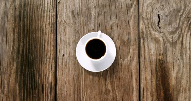 High-angle view of a cup of black coffee on a wooden table. Ideal for use in food and beverage blogs, cafe menus, social media posts related to coffee culture, or promotional materials for coffee shops.