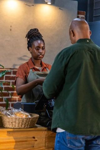 African american barista processing card payment at rustic bakery counter serving customer