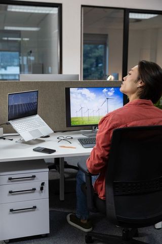 Asian woman working on renewable energy at modern office workstation with wind turbines