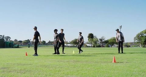 Diverse male athletes performing dynamic warm-up drills on outdoor field with coach