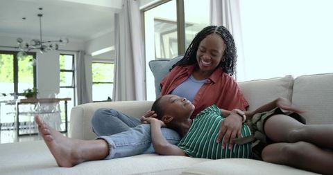 African american mother and daughter relaxing on sofa, sharing joyful bonding moment at home