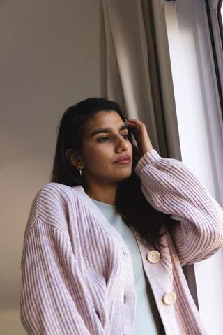 Serene woman in cozy cardigan gazing out window at home